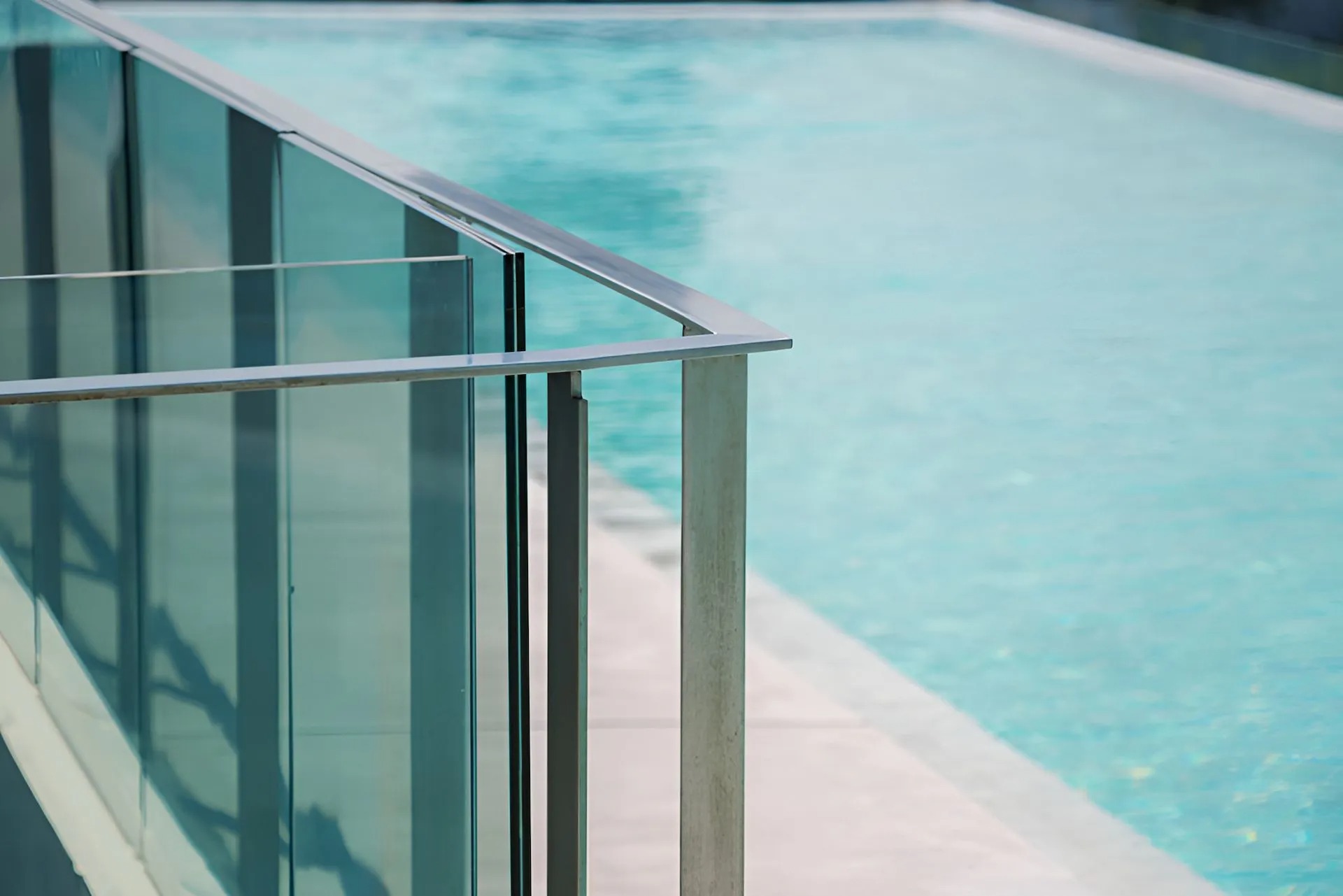 Semi-frameless glass pool fencing with stainless top rail beside a swimming pool