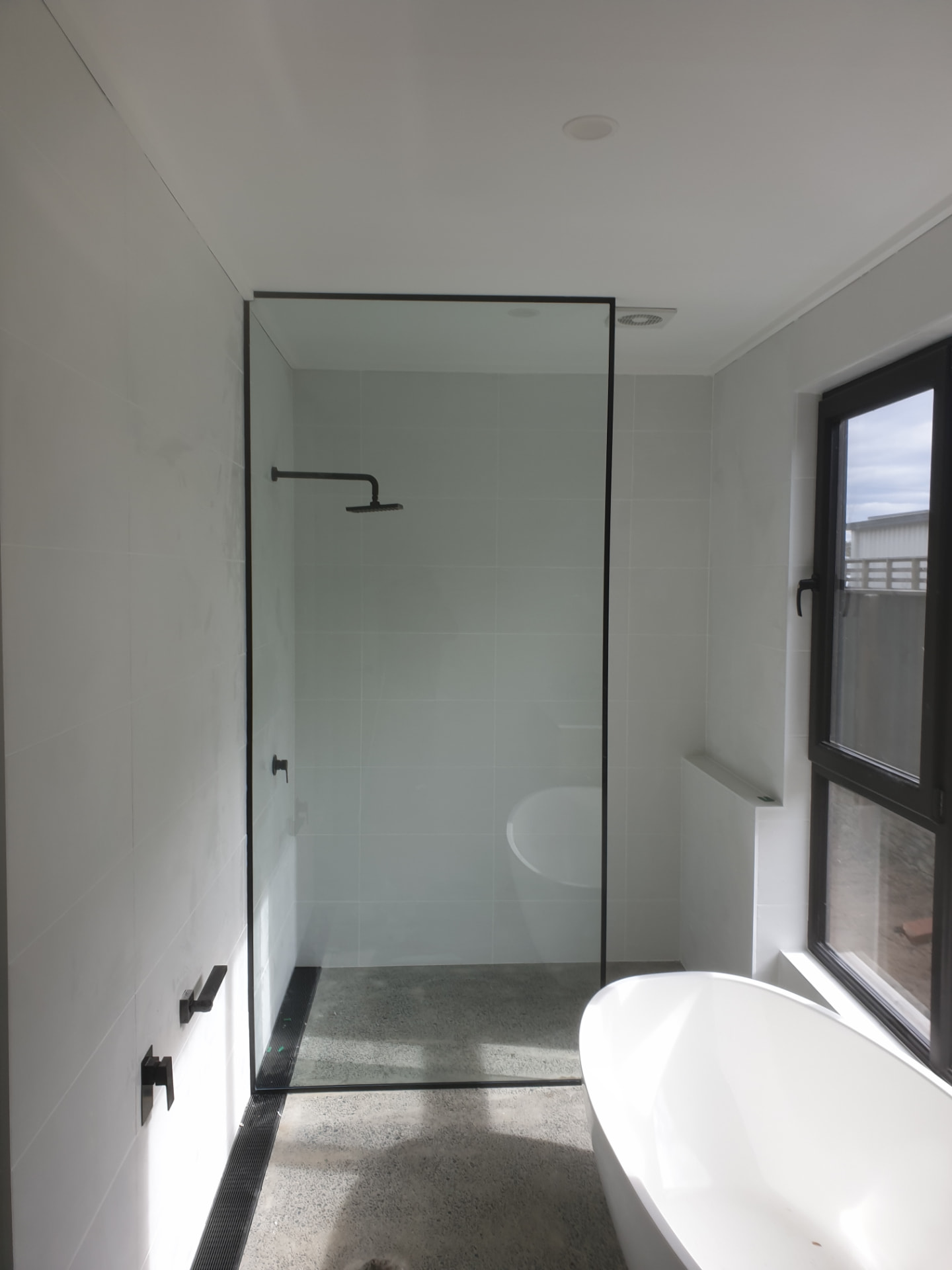 Black-framed walk-in glass shower screen beside a freestanding bath
